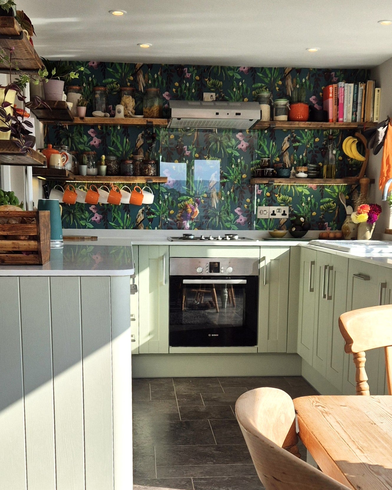 Modern kitchen with green cabinets, black appliances, and a colorful Kitito Wallpaper backsplash.