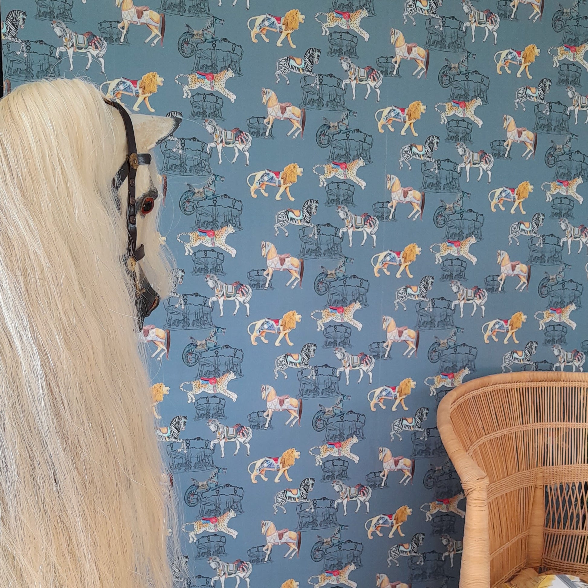 A Rocking horse and Malawi Chair with a wall behind featuring Carousel Safari wallpaper a carousel and safari-themed wallpaper.