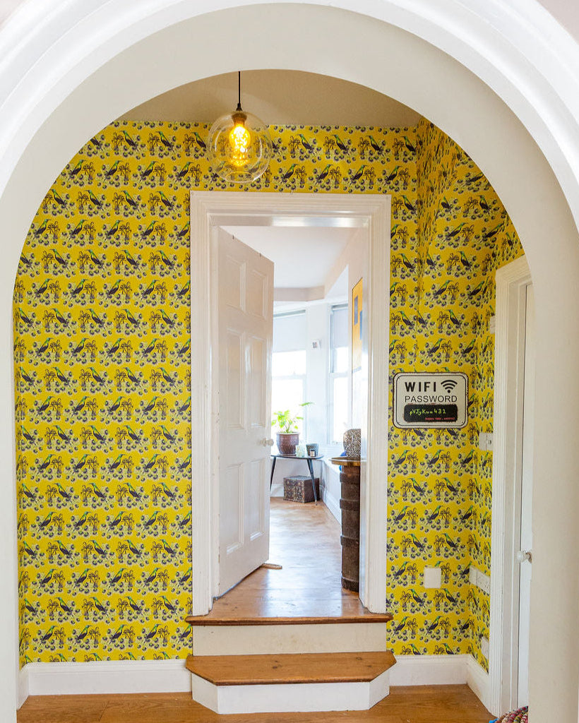 Archway with yellow floral Kirimiri wallpaper and a cat walking on a wooden floor.