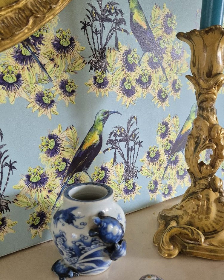 Decorative scene with a blue and white vase, gold candlestick, and floral Kirimiri wallpaper (Winter Sky - pale blue).