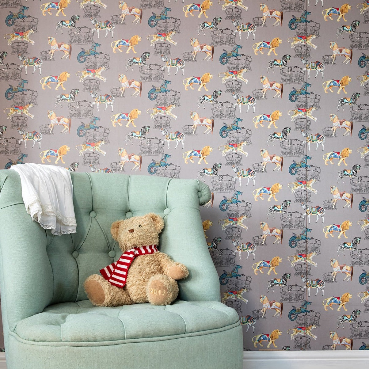 A teddy bear sitting in a green armchair with a wall behind featuring Carousel Safari wallpaper a carousel and safari-themed wallpaper.
